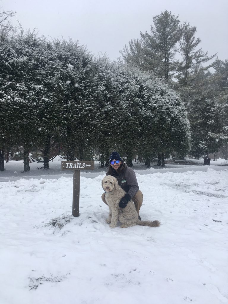 Man and dog posing in front of snowy trail sign